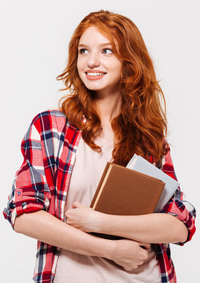 Pleased ginger woman in shirt holding books and looking away over gray background